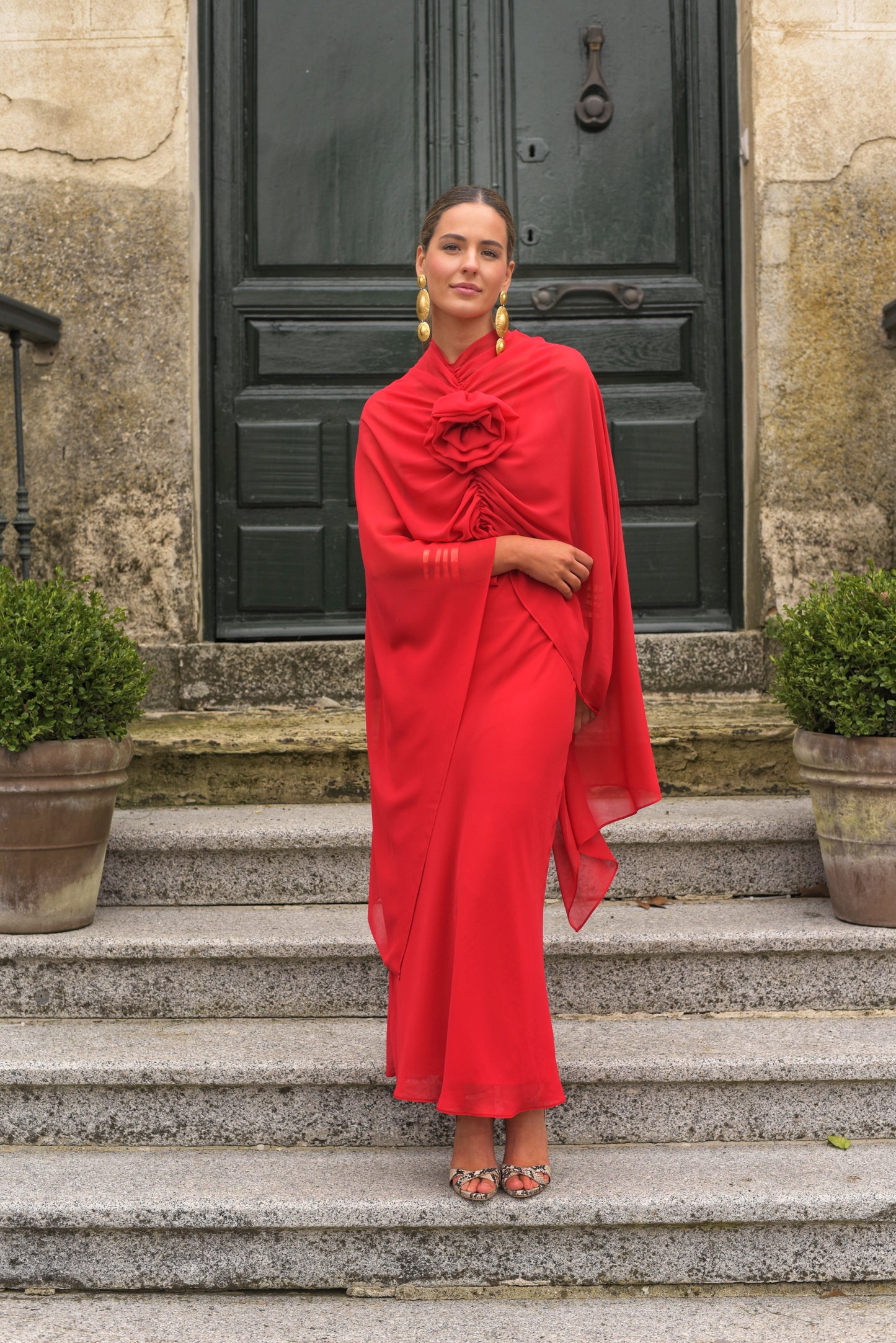 El Vestido Lady Gacela rojo es una propuesta delicada y femenina para invitadas que buscan un estilo fluido con toques sofisticados. De corte lencero, este vestido largo de fiesta presenta un elegante escote en pico tanto en el delantero como en la espalda, realzando sutilmente la silueta.
Está confeccionado en gasa ligera de tono rojo vibrante y se completa con una capita vaporosa y un broche de flor multiposición que puedes colocar en el escote central o lateral, permitiendo adaptar el look según la ocas
