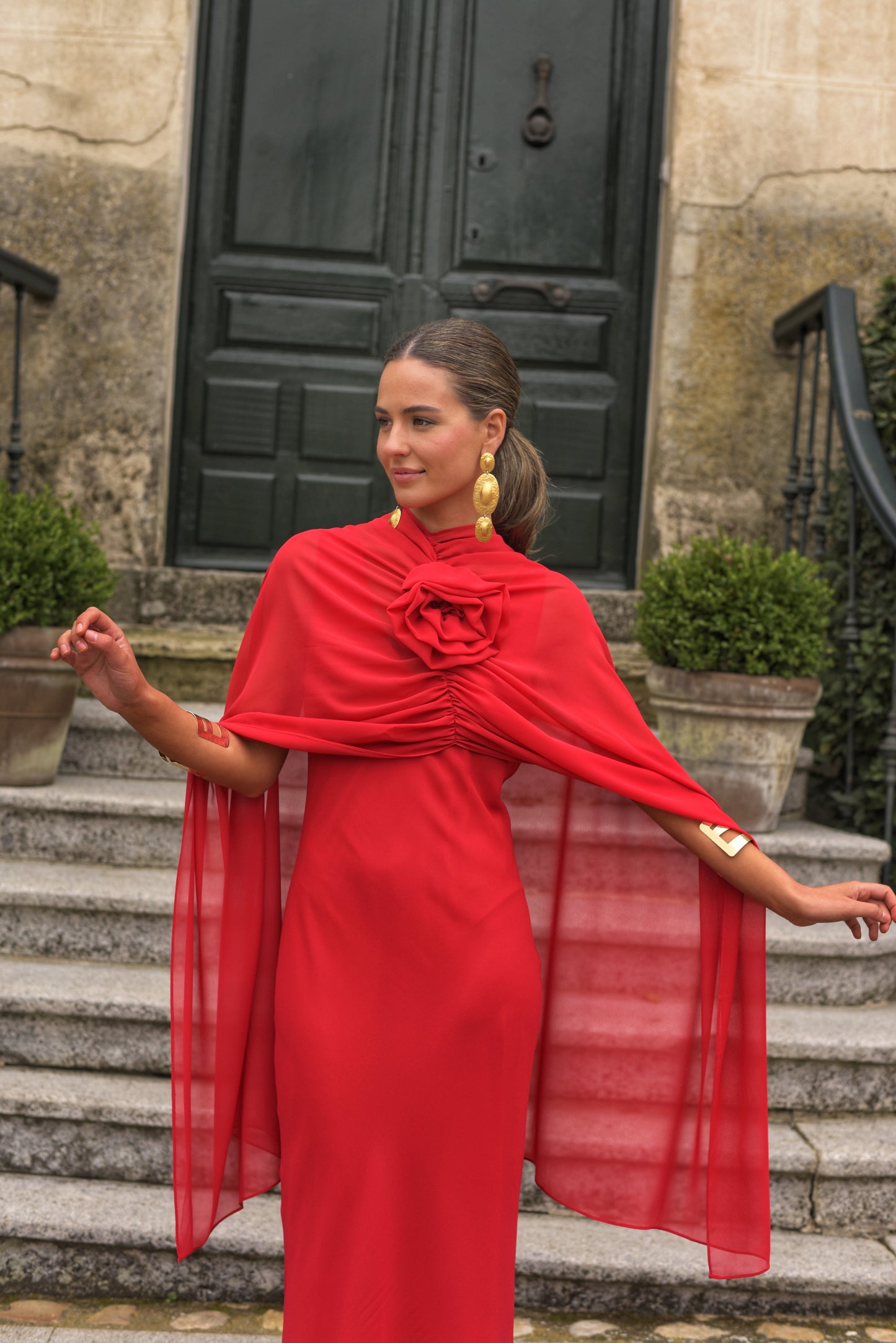El Vestido Lady Gacela rojo es una propuesta delicada y femenina para invitadas que buscan un estilo fluido con toques sofisticados. De corte lencero, este vestido largo de fiesta presenta un elegante escote en pico tanto en el delantero como en la espalda, realzando sutilmente la silueta.
Está confeccionado en gasa ligera de tono rojo vibrante y se completa con una capita vaporosa y un broche de flor multiposición que puedes colocar en el escote central o lateral, permitiendo adaptar el look según la ocas