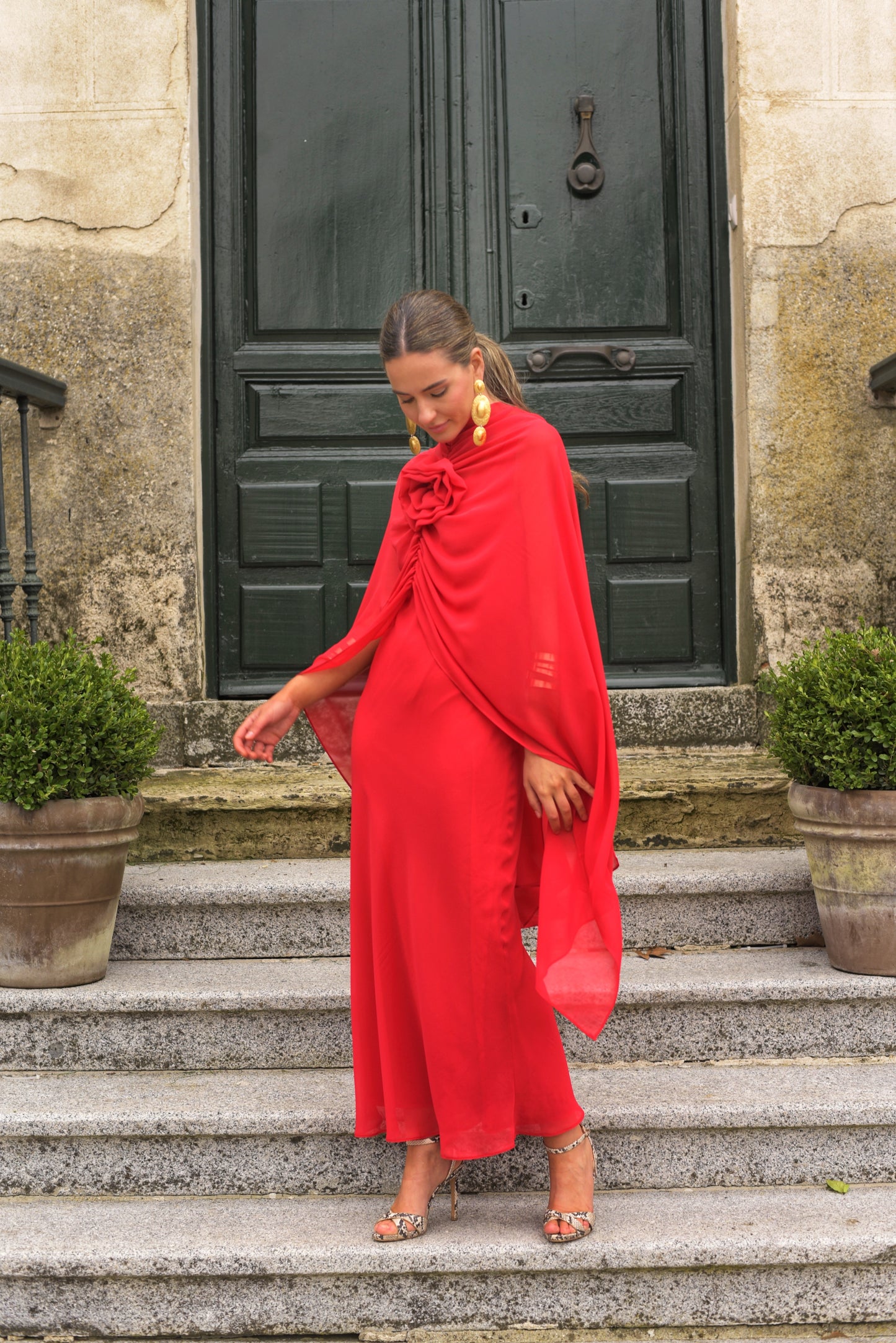 El Vestido Lady Gacela rojo es una propuesta delicada y femenina para invitadas que buscan un estilo fluido con toques sofisticados. De corte lencero, este vestido largo de fiesta presenta un elegante escote en pico tanto en el delantero como en la espalda, realzando sutilmente la silueta.
Está confeccionado en gasa ligera de tono rojo vibrante y se completa con una capita vaporosa y un broche de flor multiposición que puedes colocar en el escote central o lateral, permitiendo adaptar el look según la ocas