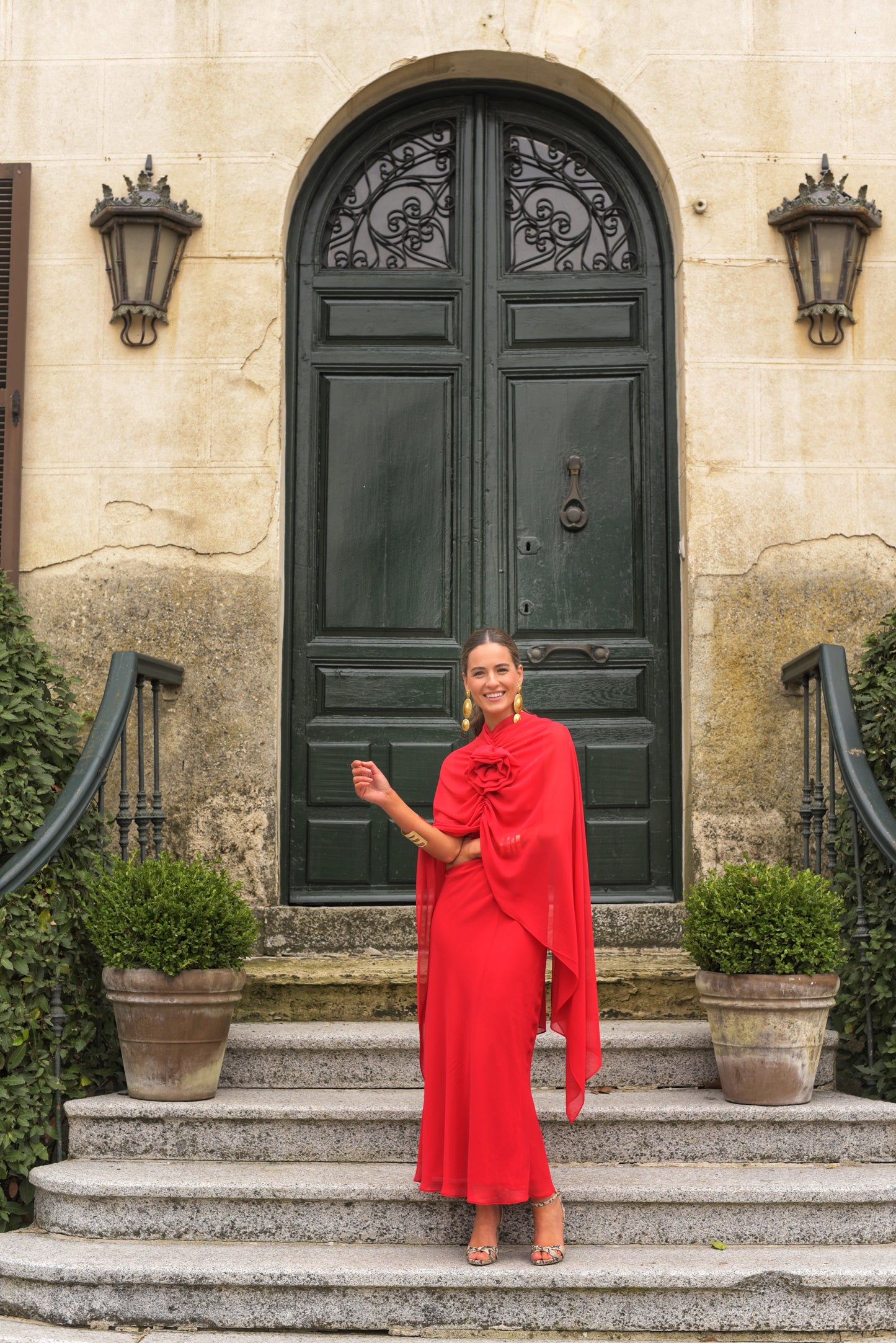 El Vestido Lady Gacela rojo es una propuesta delicada y femenina para invitadas que buscan un estilo fluido con toques sofisticados. De corte lencero, este vestido largo de fiesta presenta un elegante escote en pico tanto en el delantero como en la espalda, realzando sutilmente la silueta.
Está confeccionado en gasa ligera de tono rojo vibrante y se completa con una capita vaporosa y un broche de flor multiposición que puedes colocar en el escote central o lateral, permitiendo adaptar el look según la ocas