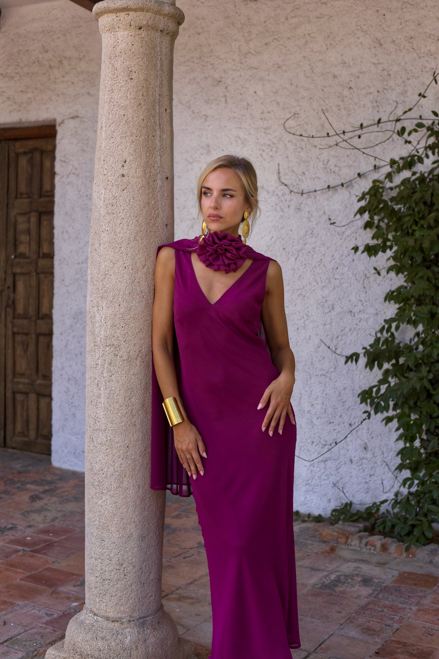 Vestido de Fiesta largo, lencero con escote de pico delante y en espalda. Con capita y broche de flor multiposición que da mucho juego y se puede colocar en el centro del escote o en un lateral.Confeccionado en gasa tono berenjena.