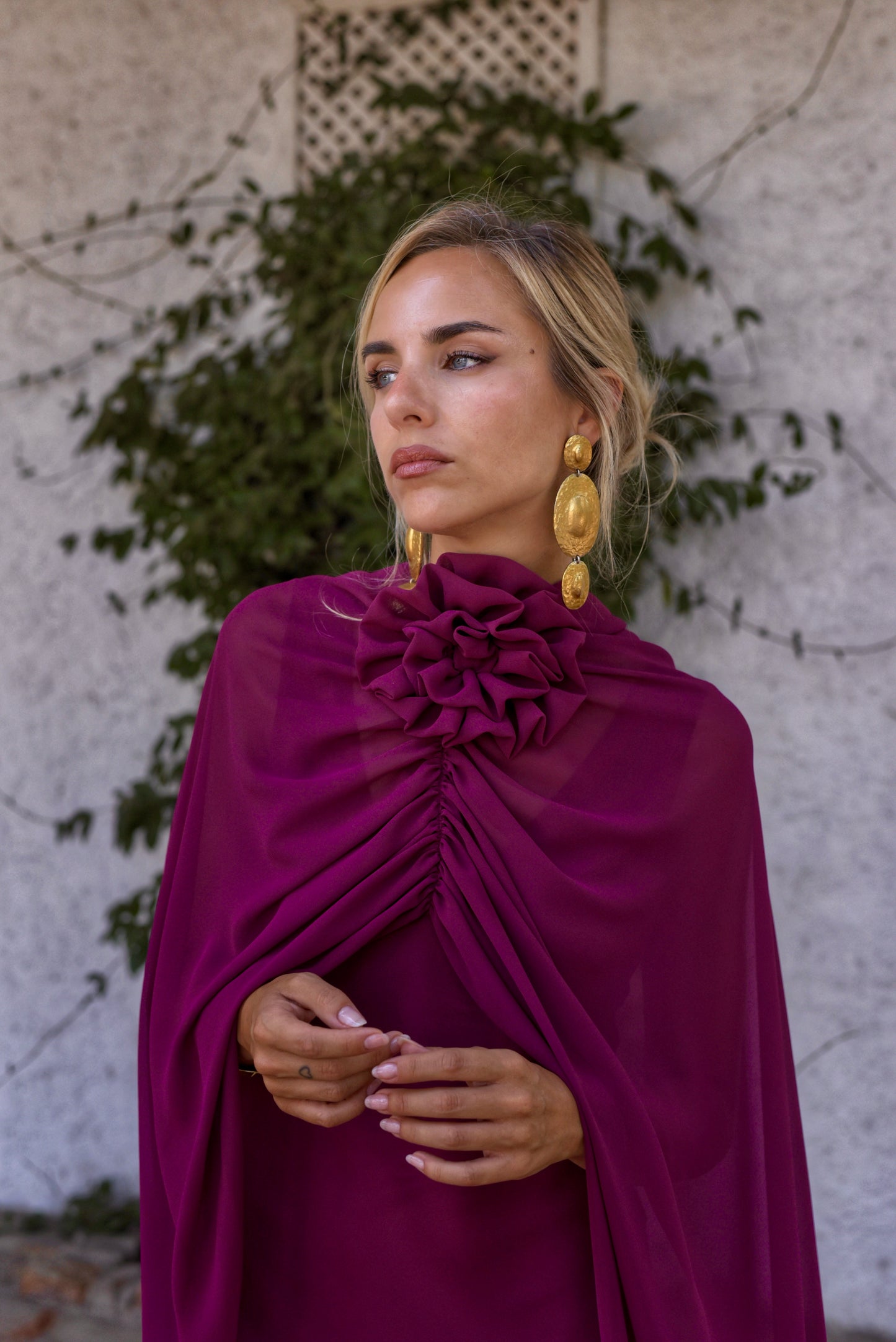 Vestido de Fiesta largo, lencero con escote de pico delante y en espalda. Con capita y broche de flor multiposición que da mucho juego y se puede colocar en el centro del escote o en un lateral.Confeccionado en gasa tono berenjena.